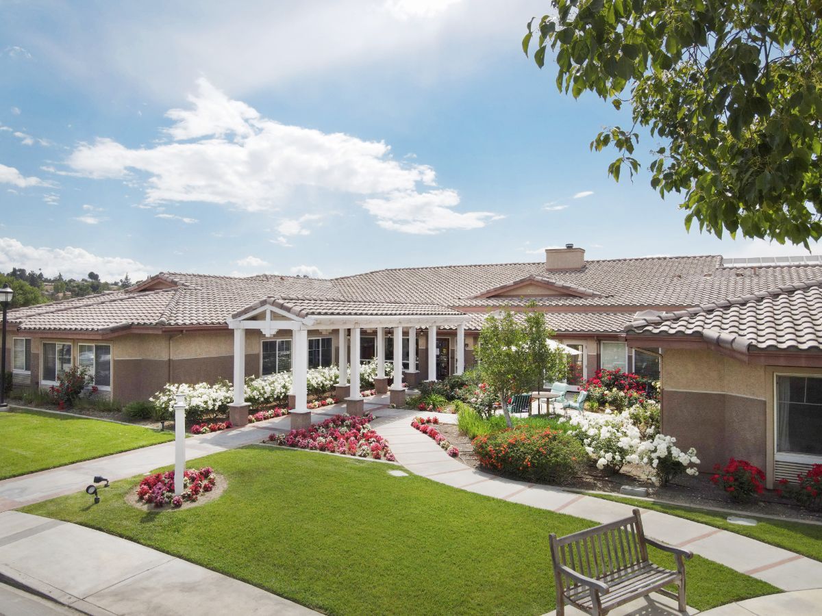 A beautiful house with a landscaped garden, featuring vibrant flowers and a peaceful bench under a clear sky.