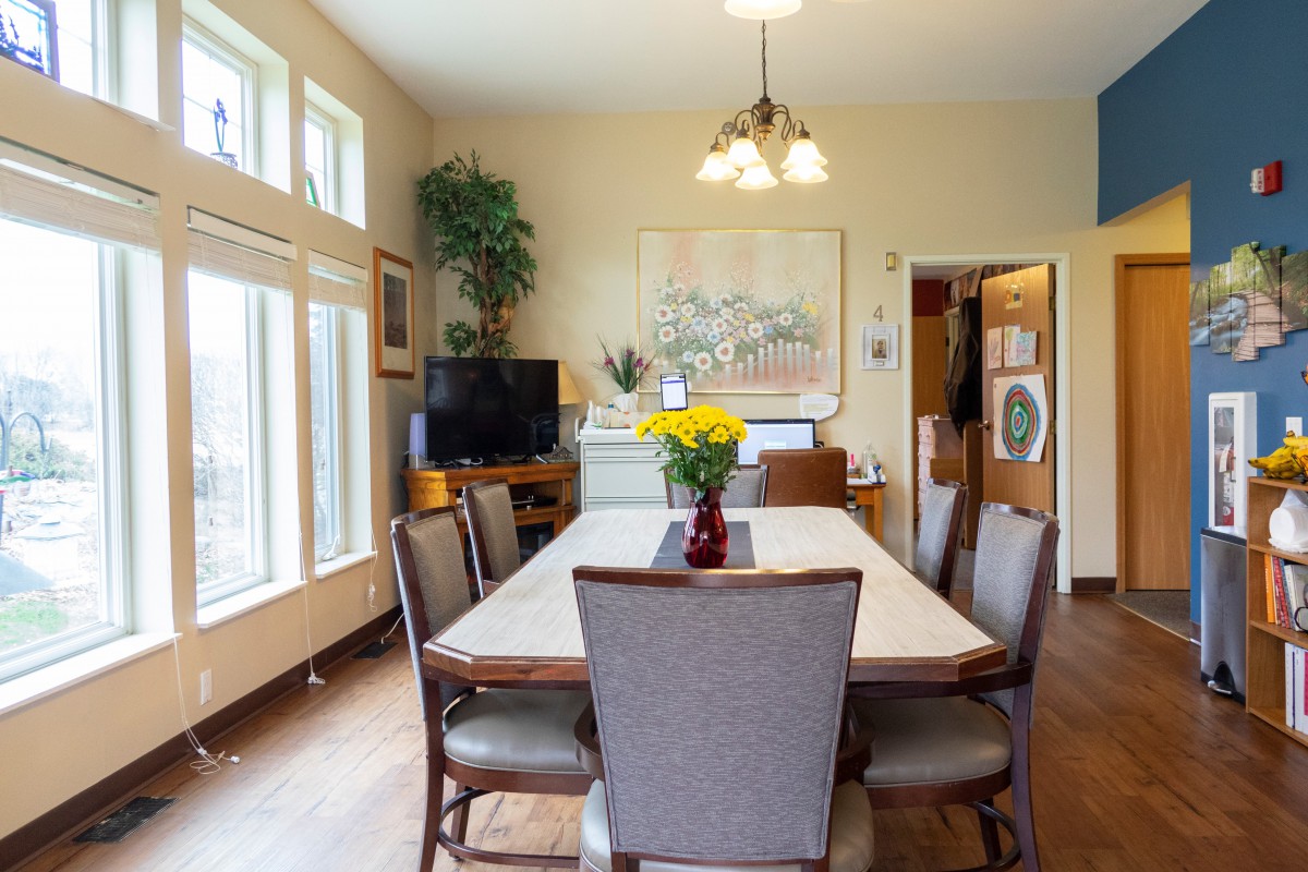 A cozy dining room with a large table and chairs, decorated with artwork, plants, and warm lighting.