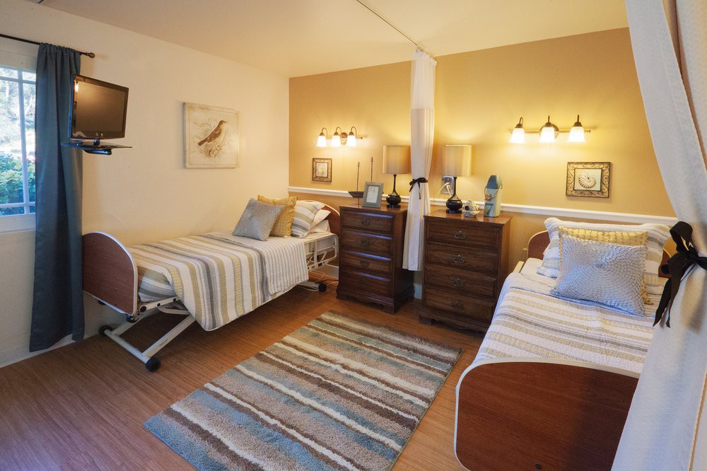 A well-organized hospital room with two beds separated by a curtain, featuring warm lighting and cozy decor.