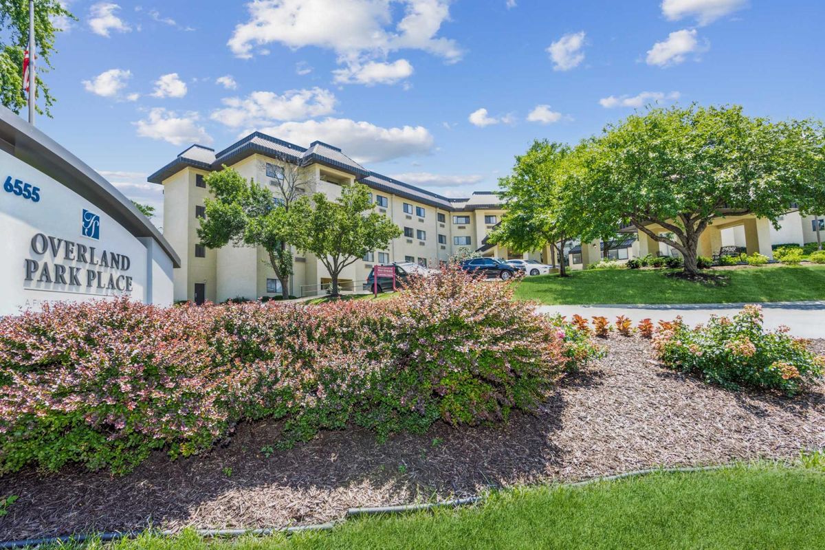 A scenic view of an apartment building surrounded by lush greenery and a partly cloudy sky.