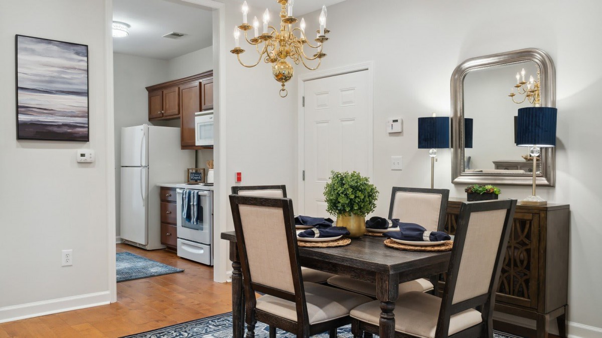 A cozy dining area with a table set for four, adjacent to a kitchen featuring wooden cabinetry and modern appliances.