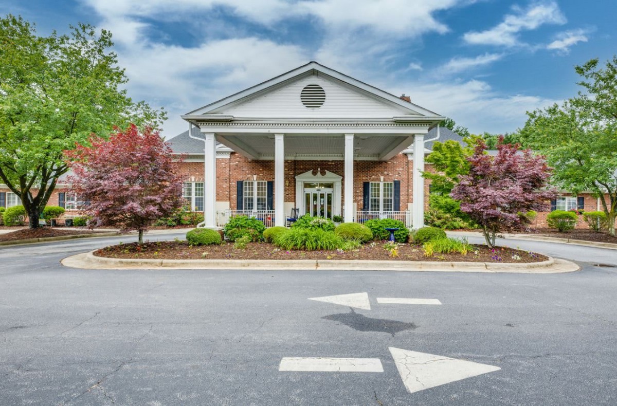 A traditional brick building with white columns at the entrance, surrounded by landscaped greenery and trees.