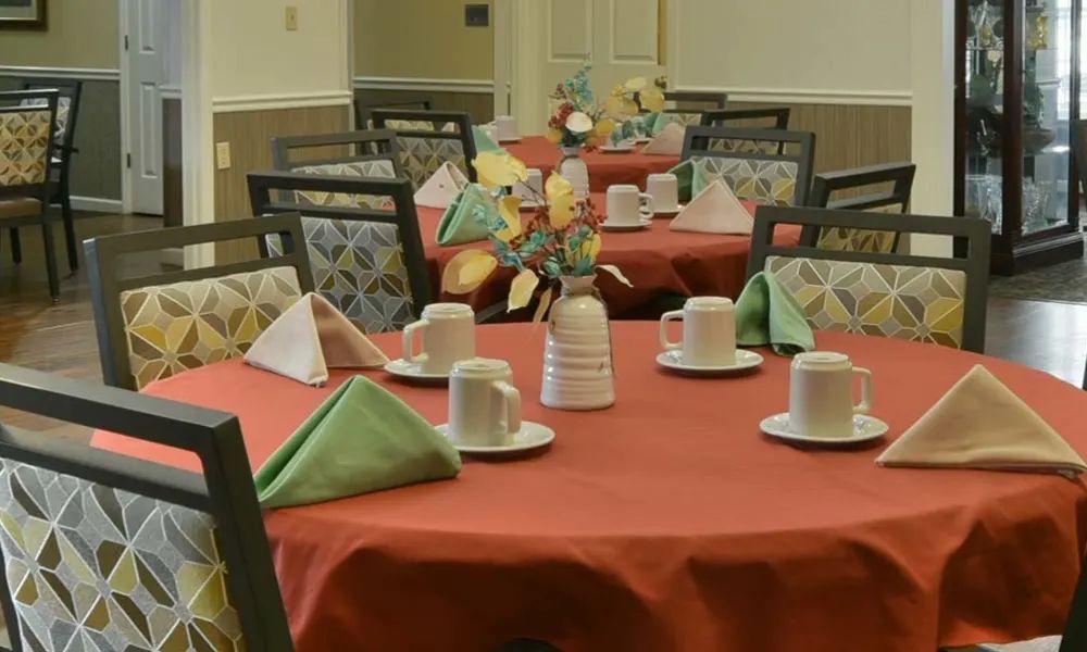 A neatly arranged dining table with a red tablecloth, cups, and decorative centerpiece in a dining room.