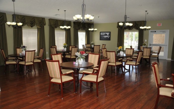 A well-lit dining room featuring wooden floors, multiple tables and chairs, with elegant chandeliers and curtains.