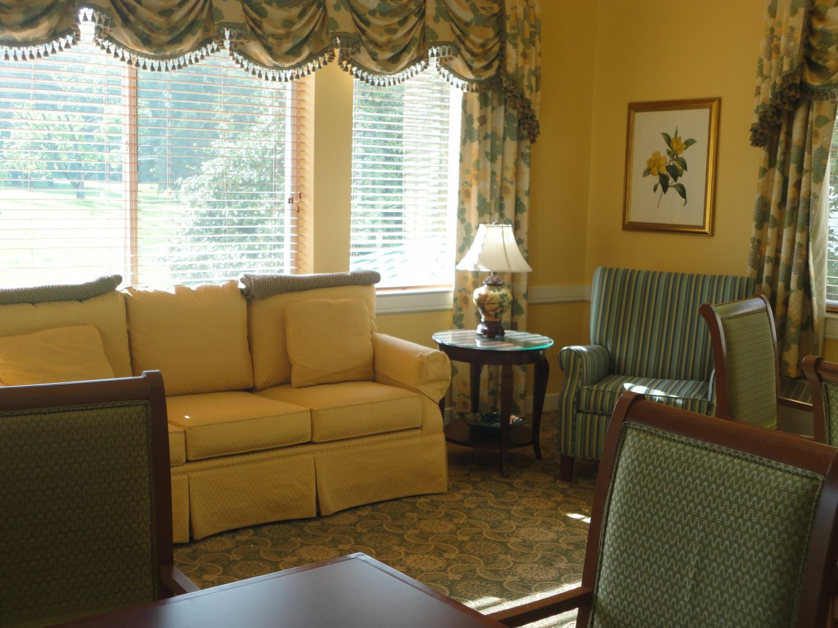 A cozy living room with yellow walls, featuring a sofa, armchair, and a table lamp by the window.