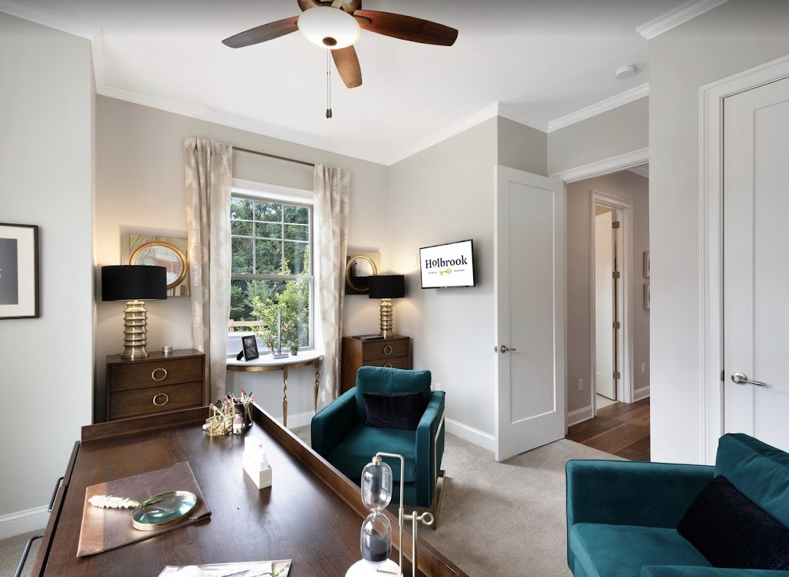 A stylish home office featuring a wooden desk, comfortable teal chairs, and large windows allowing natural light.