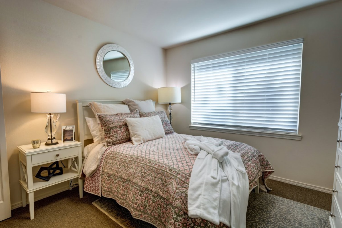A cozy bedroom with patterned bedding, a wall mirror, and soft lighting.