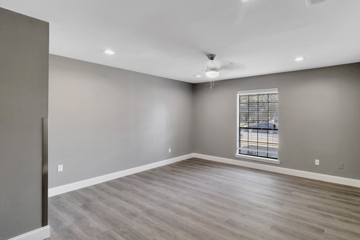 A spacious empty room with modern flooring, a window, and a ceiling fan.
