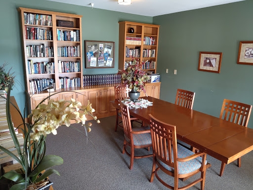 A cozy library and dining area featuring wooden bookshelves filled with books, a polished dining table surrounded by chairs, and decorative plants enhancing the space.