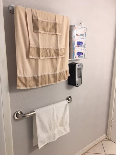 A bathroom wall with a towel rack, towels, and a soap dispenser.