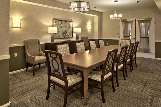 A spacious dining room featuring a long wooden table surrounded by elegantly designed chairs, complemented by soft lighting for a warm ambiance.