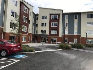 A modern apartment building with a parking lot in the foreground.