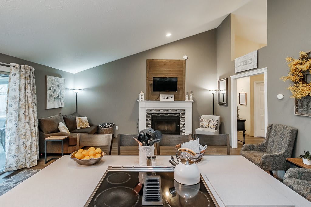 A modern living room with a kitchen island, cozy seating, and a fireplace under a vaulted ceiling.