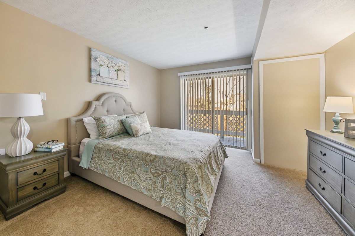 A cozy bedroom with a bed, side table, and a window with blinds.