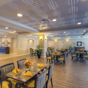 A spacious and elegantly decorated dining room with arranged tables and chairs, adorned with centerpieces of vibrant flowers.