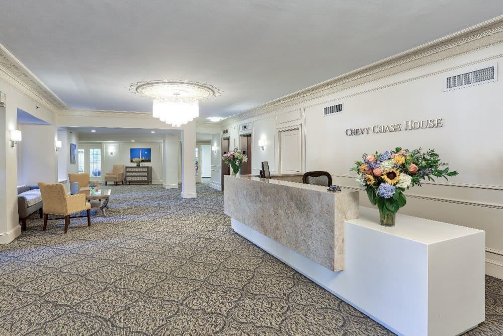 A well-lit hotel lobby featuring a reception desk with floral arrangements and a chandelier.