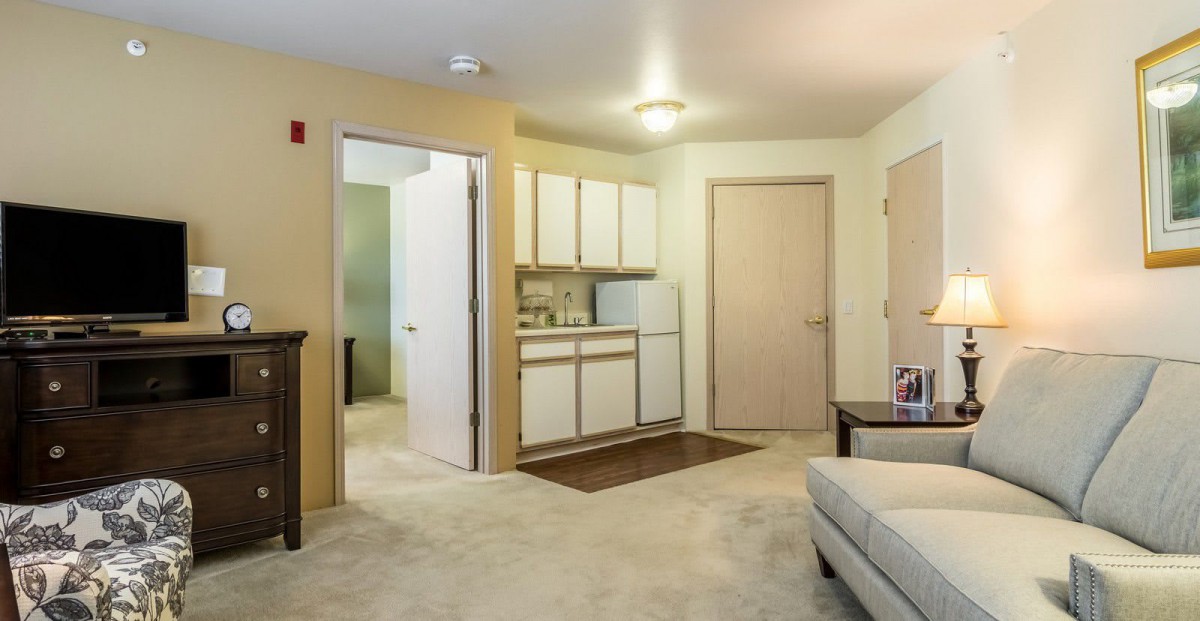 A cozy studio apartment featuring a kitchenette and a small living area with beige walls.