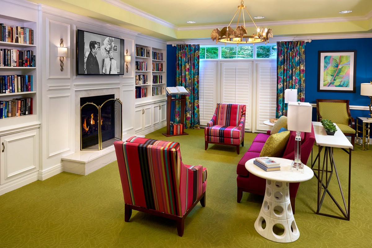 A vibrant and cozy living room featuring a fireplace, striped chairs, and a TV with classic black-and-white movies.