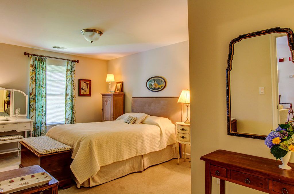 A cozy bedroom with traditional decor, featuring a comfortable bed, nightstands with lamps, and a mirror.
