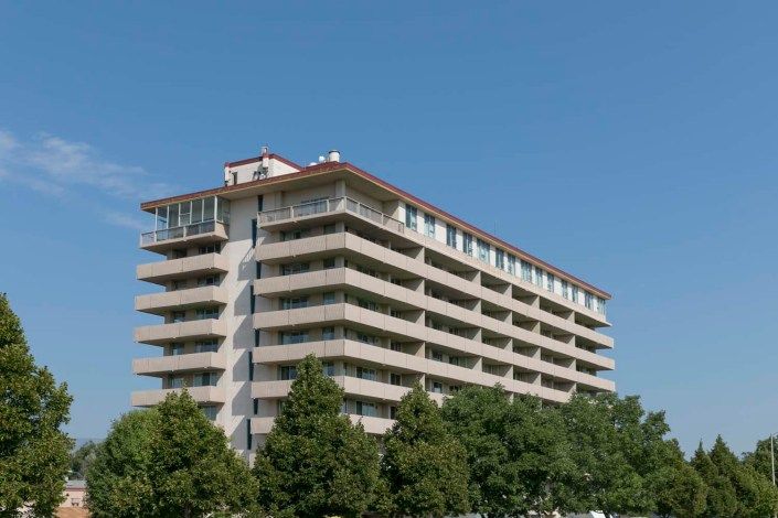 A modern apartment building surrounded by trees under a clear blue sky.