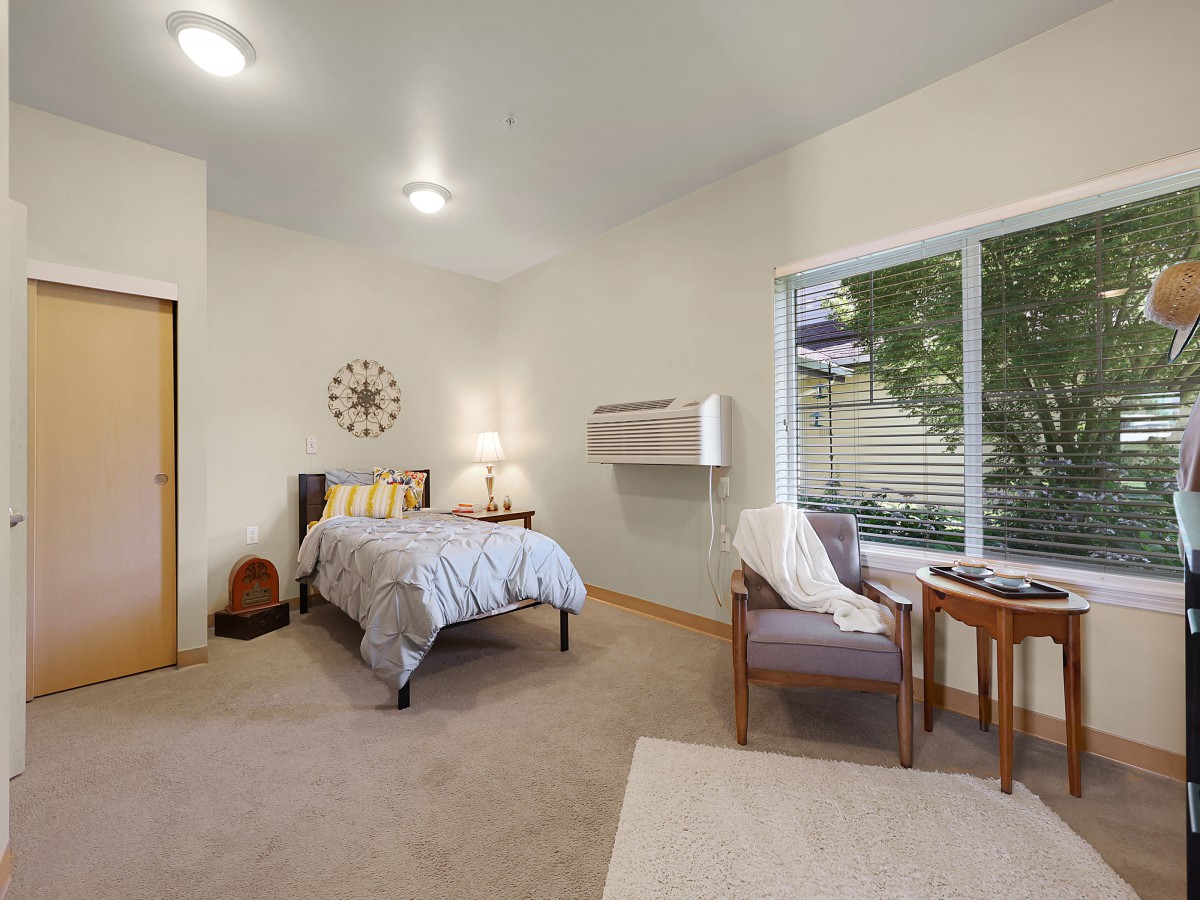 A cozy bedroom with a bed, chairs, and a large window letting in natural light.