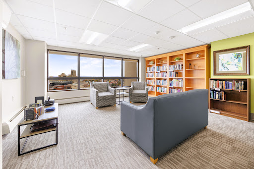 A serene office space featuring comfortable seating, a bookshelf filled with books, and large windows offering a city view.