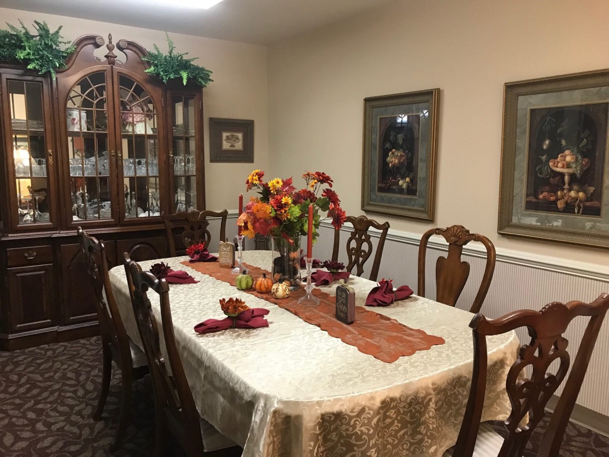 A dining room with an autumn-themed table setting, featuring a decorative centerpiece and surrounded by chairs.