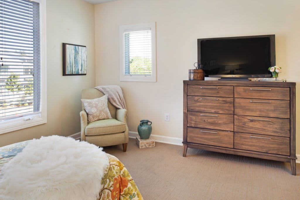 A cozy bedroom with a chair, dresser, and television.
