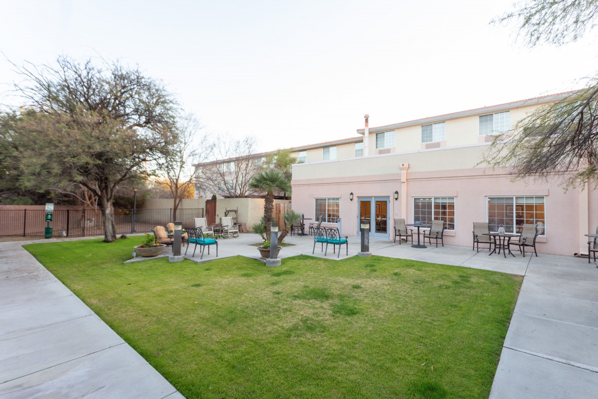A backyard with a lush lawn, patio seating, and trees surrounding a residential house.