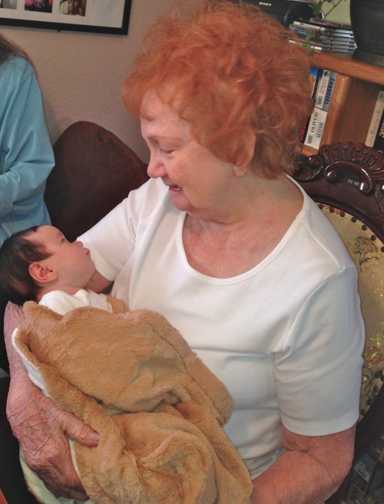 An elderly woman lovingly holds a baby in her arms inside a cozy room.