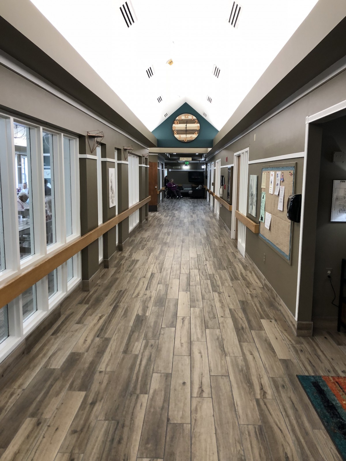 A long hallway with wooden flooring and large windows on one side.