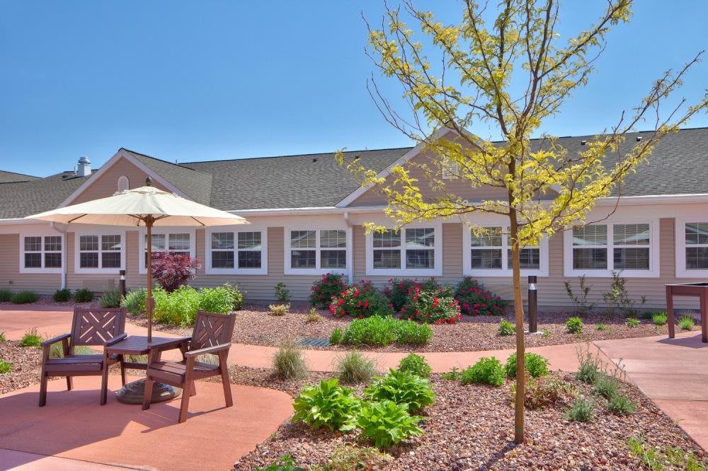 A sunny outdoor patio area with garden landscaping and seating in front of a building.