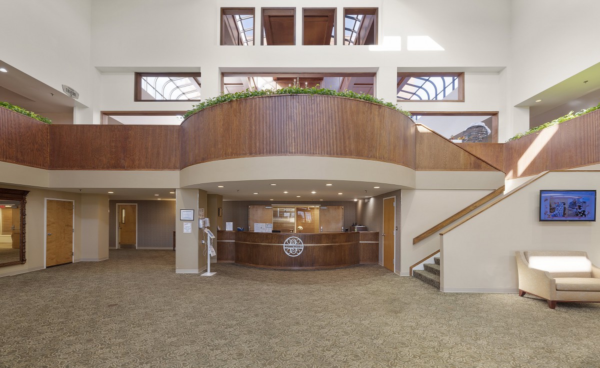 A spacious reception area with wood paneling and a central desk, flanked by staircases.