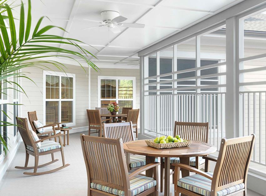 A cozy patio area with tables and chairs, featuring plants and a ceiling fan.