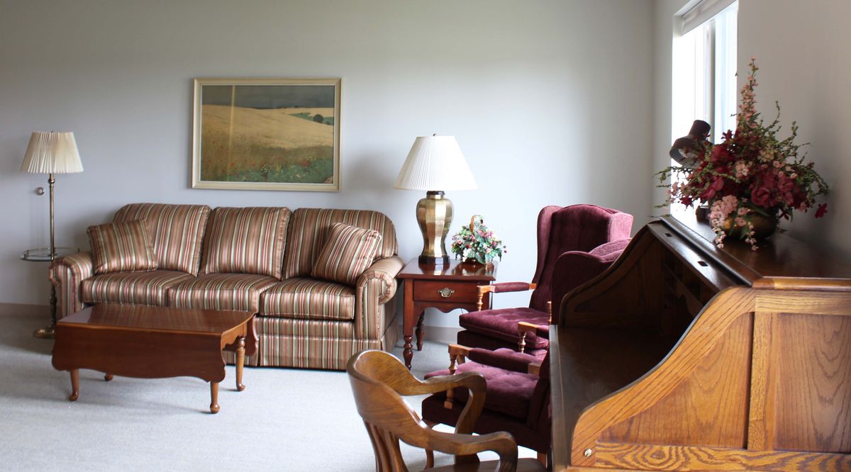 A cozy living room with a striped sofa, maroon armchairs, and a decorative table lamp.