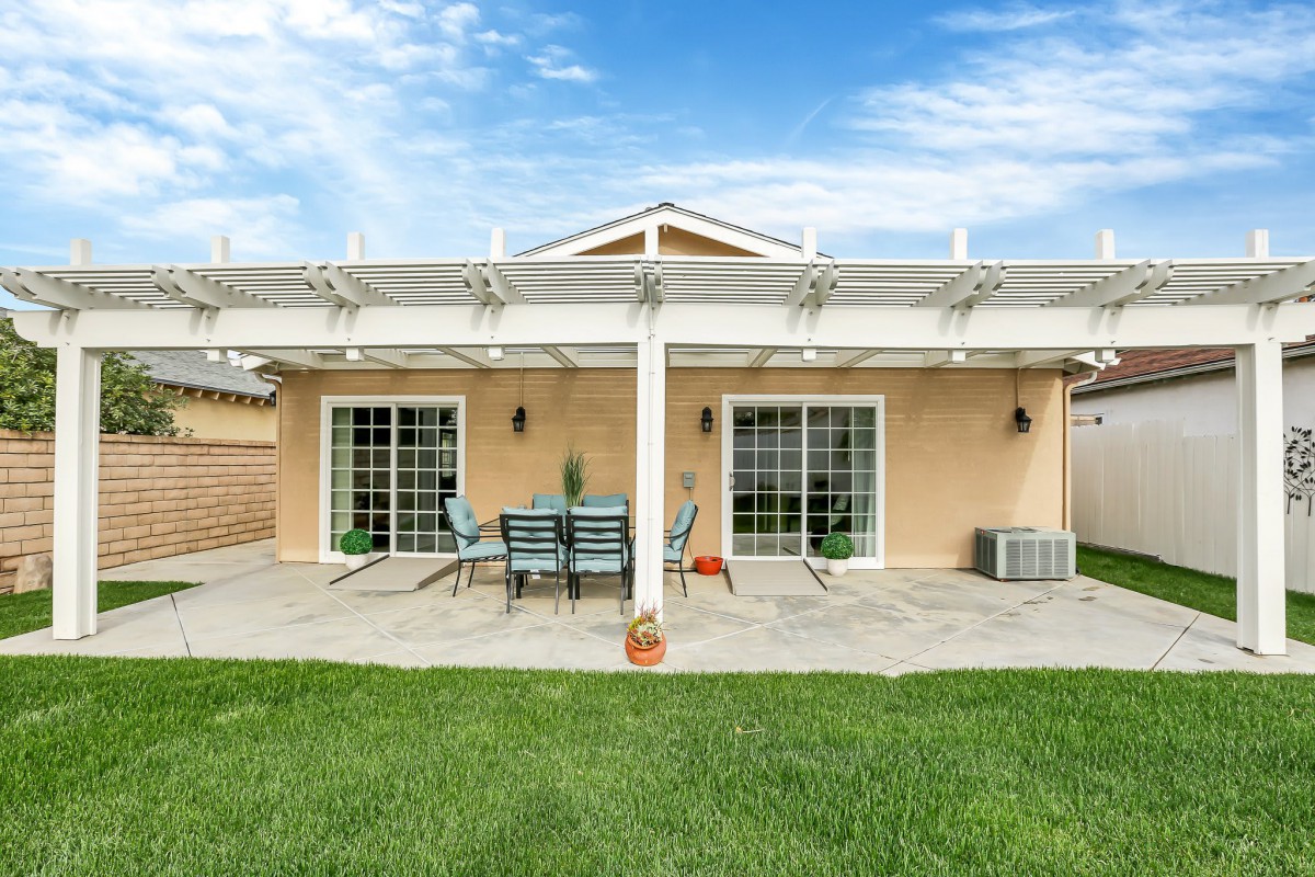 A backyard patio featuring outdoor furniture under a pergola with sliding glass doors leading to the house.