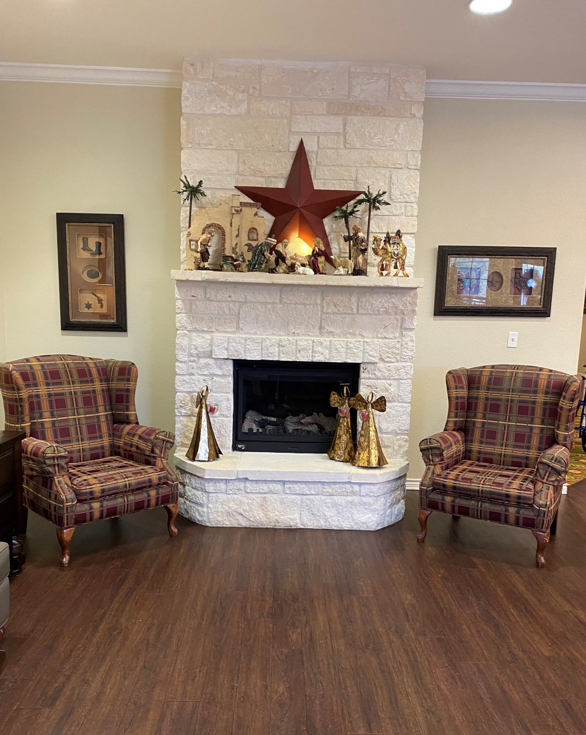 A cozy living room with a white stone fireplace, flanked by two plaid chairs and decorated with a large star on the mantel.