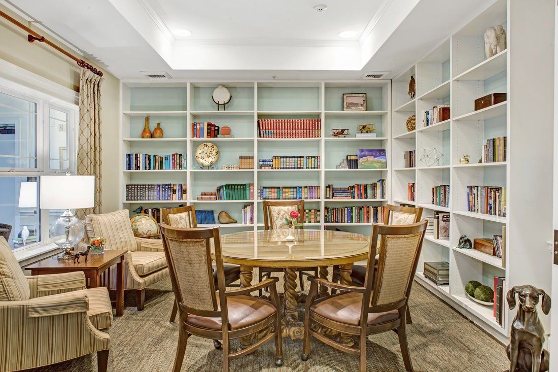 A cozy reading room with a round table and chairs surrounded by bookshelves.