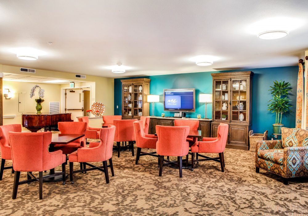 A cozy seating area with vibrant orange chairs, a television, and bookshelves in a well-decorated lobby.