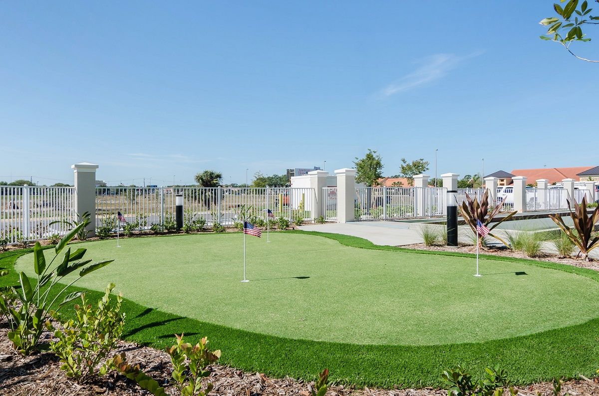 A sunny day at a well-maintained outdoor putting green, surrounded by a landscaped area.