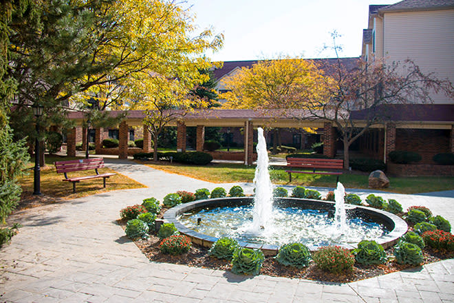 A serene courtyard featuring a central fountain surrounded by greenery and trees with autumn foliage.
