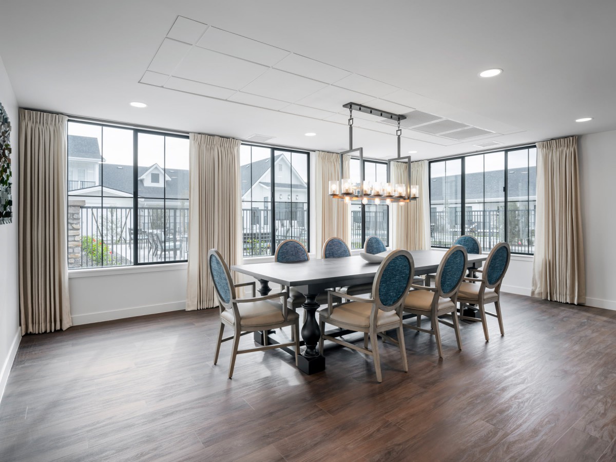 A spacious dining room featuring a large table with elegant chairs, surrounded by large windows and highlighted by a modern chandelier.