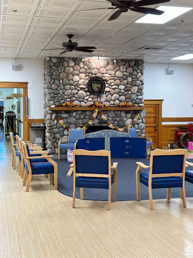 A cozy waiting area featuring wooden chairs arranged around a stone fireplace.