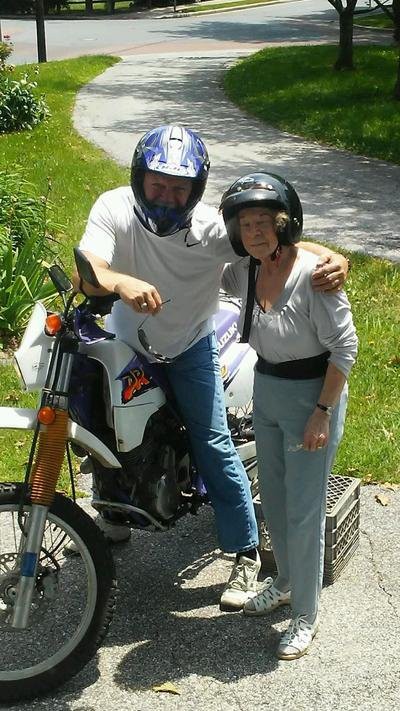 Two people pose with a motorcycle, both wearing helmets outdoors.