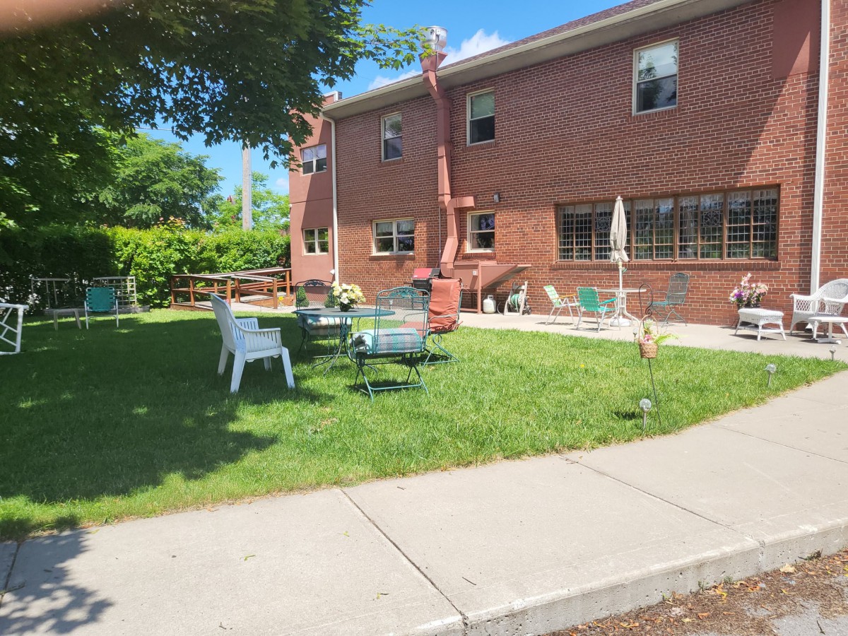 A cozy outdoor seating area with chairs and tables on a lawn next to a brick building.