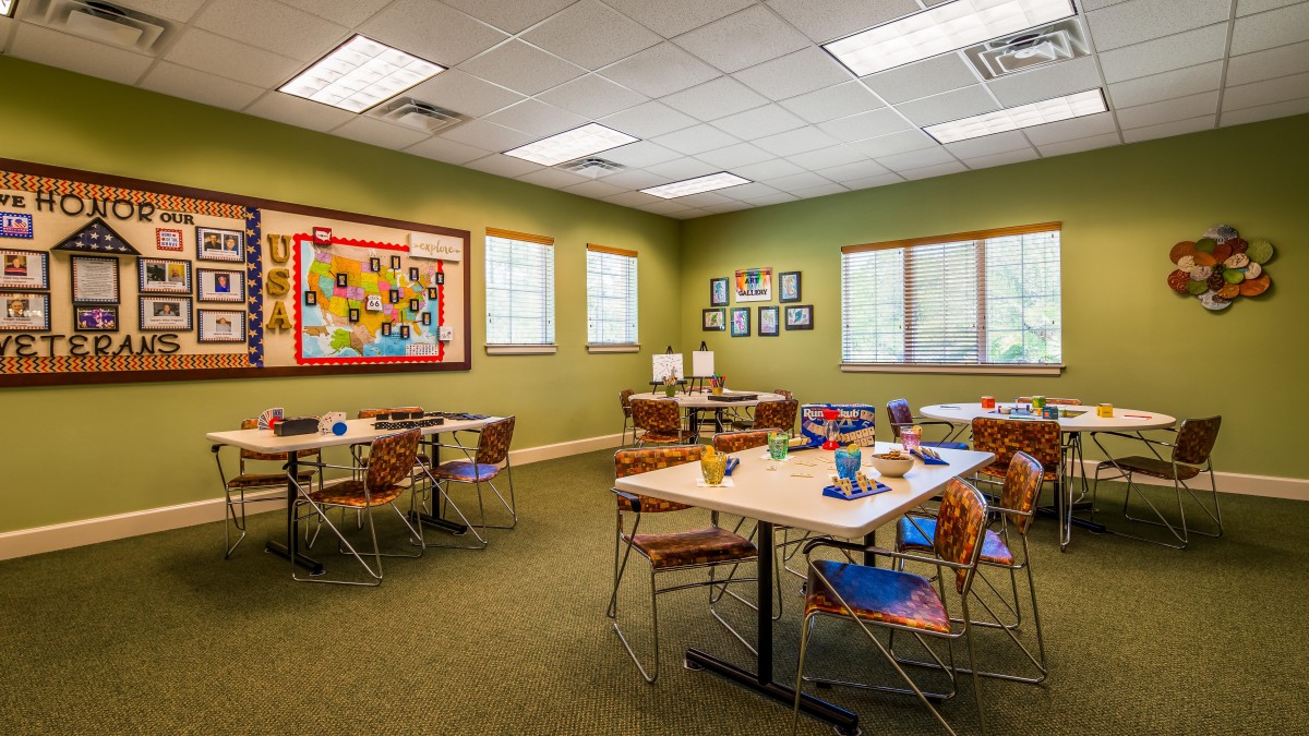 A bright and colorful classroom with tables and chairs, featuring art supplies and educational decorations on the walls.