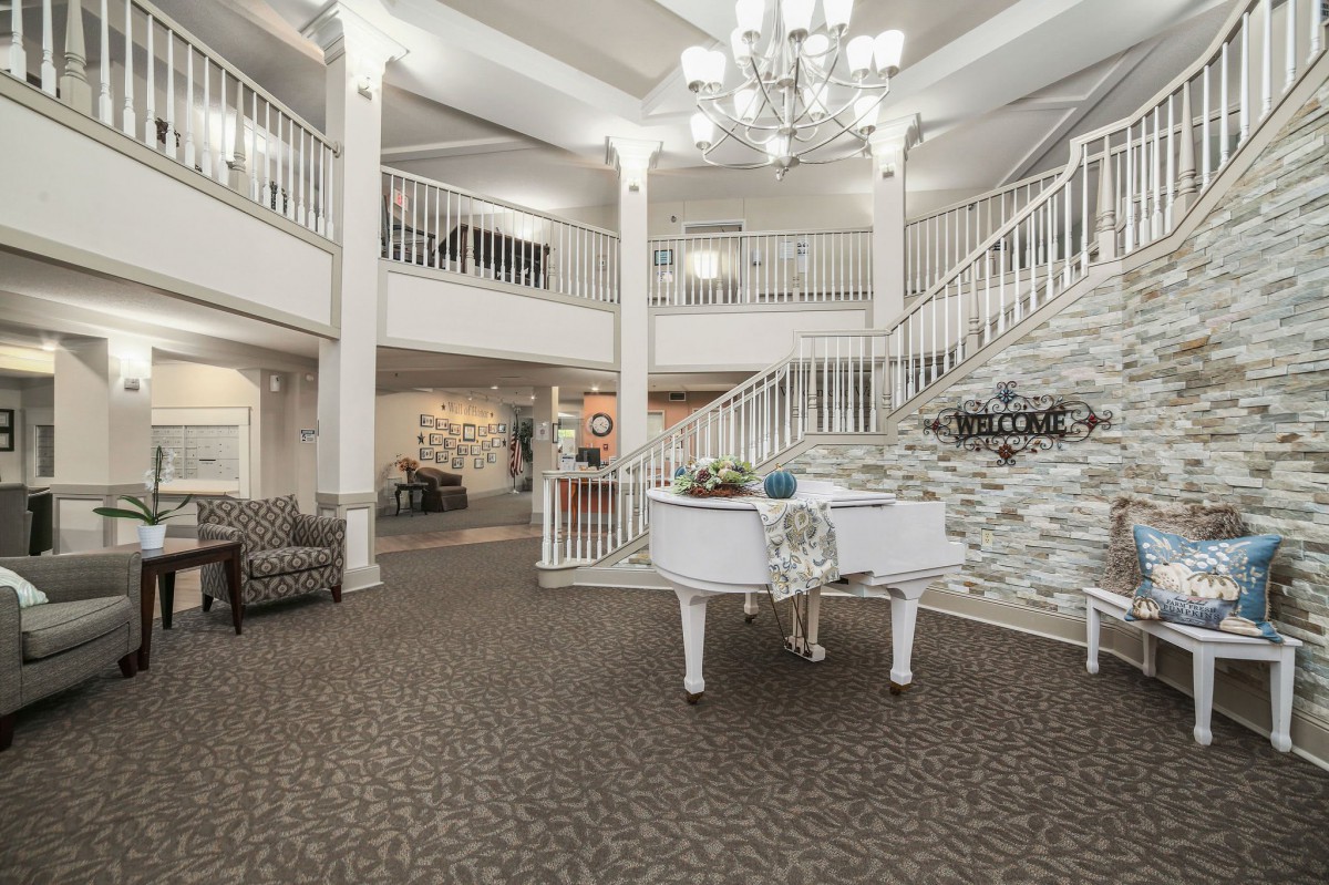 An elegant lobby featuring a grand piano, chandelier, and ornate staircase.