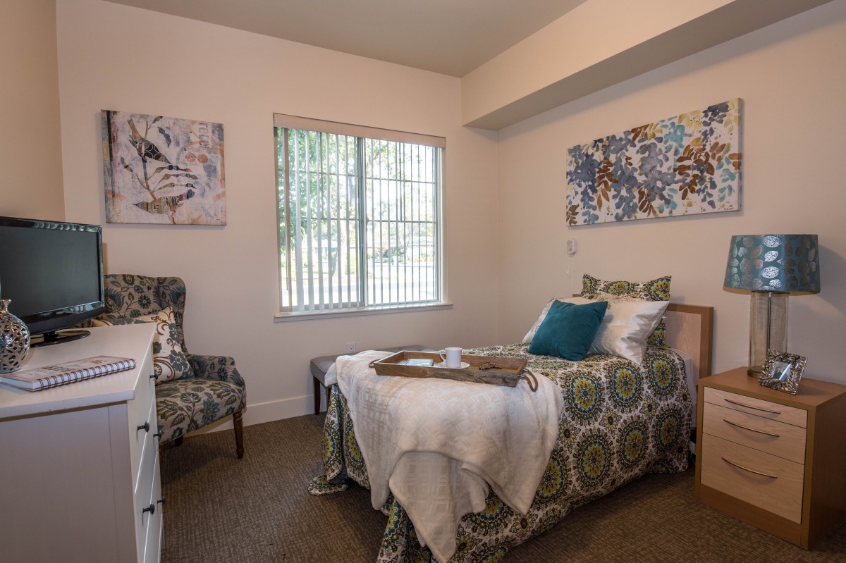 A cozy bedroom with patterned bedding, an armchair, and decorative wall art.