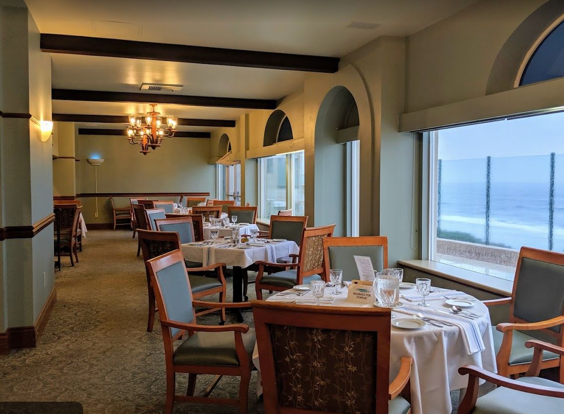 An elegant restaurant dining room with ocean views and neatly set tables.