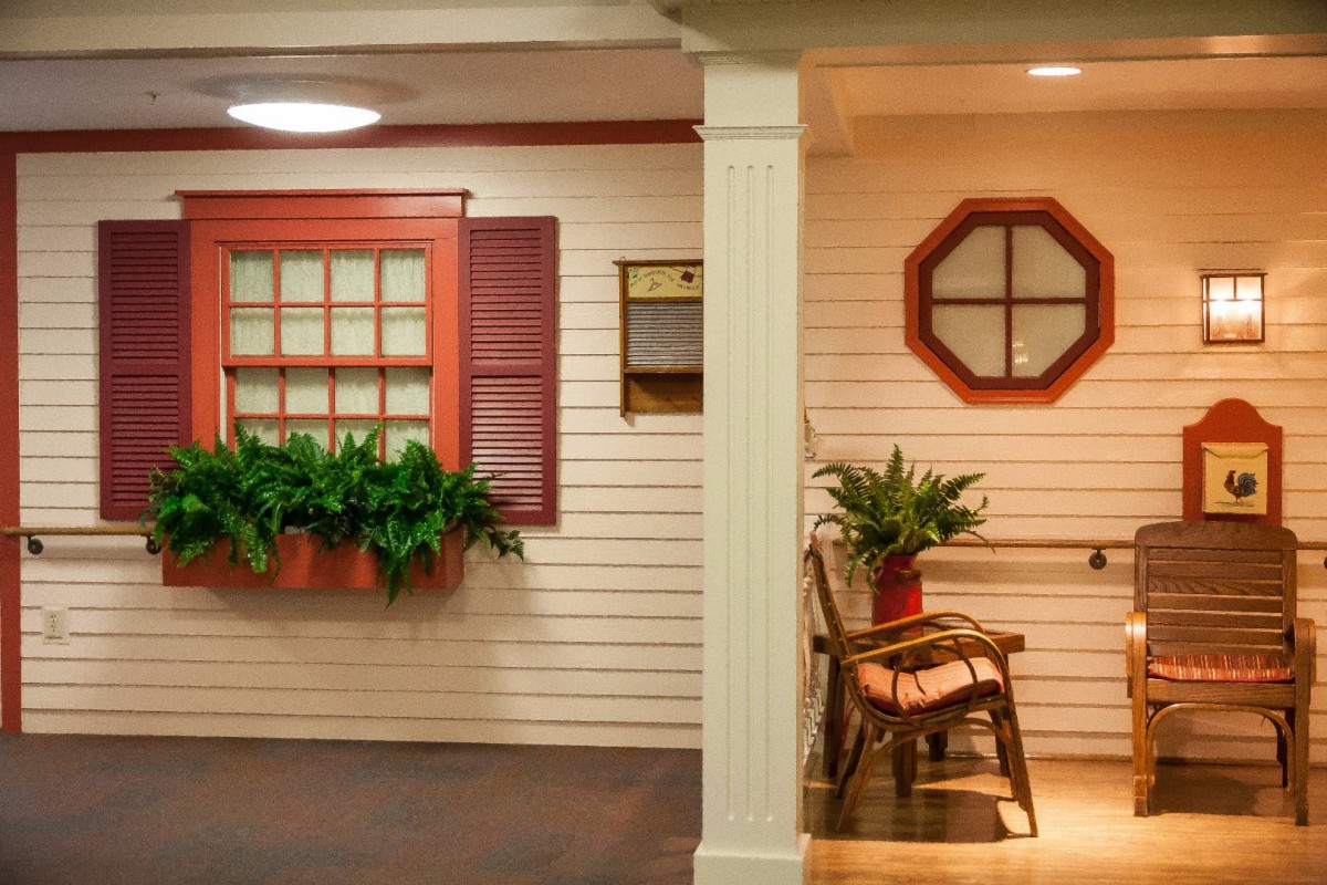 A cozy indoor porch area featuring a rocking chair, potted plants, and decorative windows with shutters.